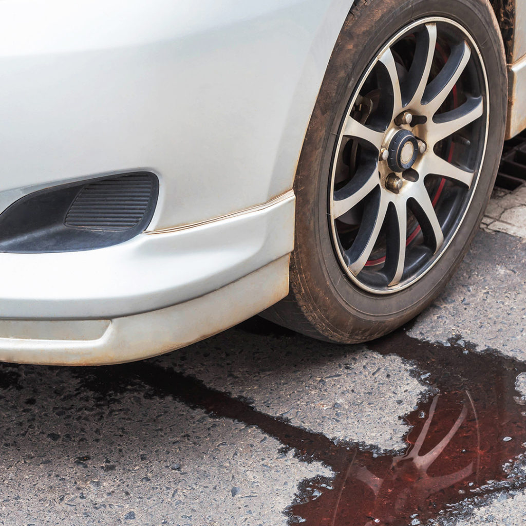 Red transmission fluid leaking out from under a white car.