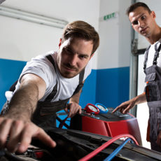 two mechanics working under hood of car